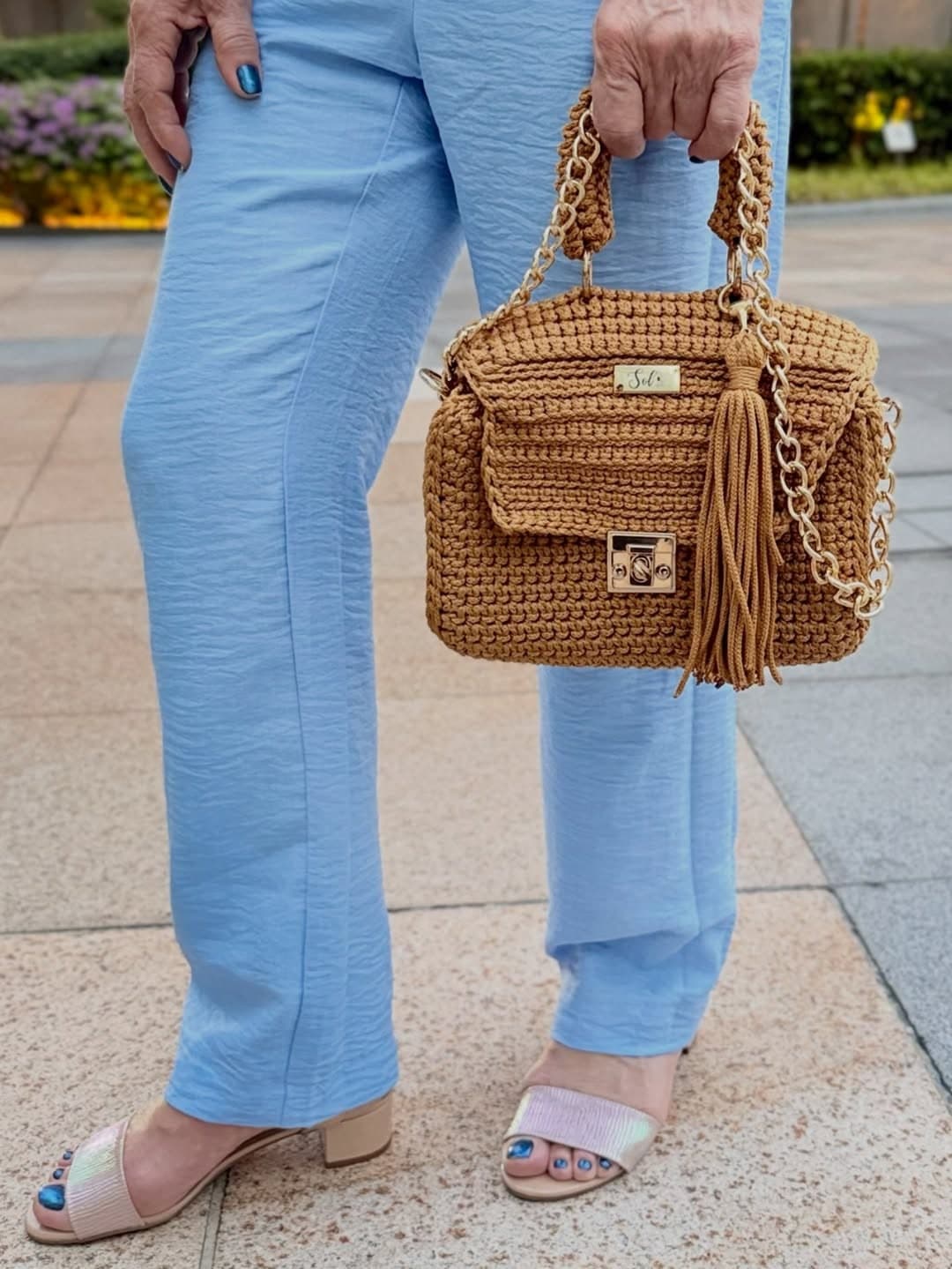 Detalhe da bolsa Siena caramelo na mão, com calça azul-clara