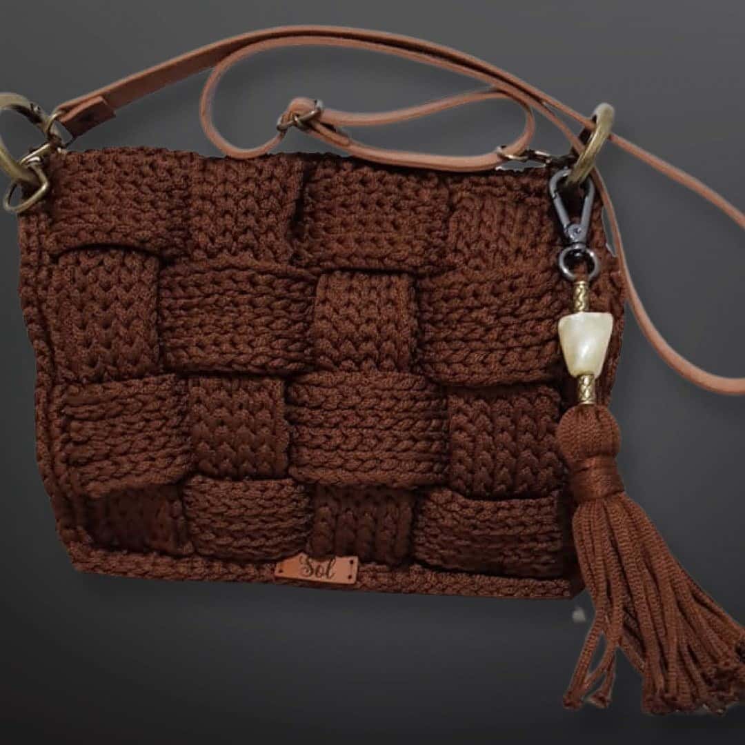 Bolsa Atenas marrom em trançado de crochê, com tassel e alça tiracolo tipo couro