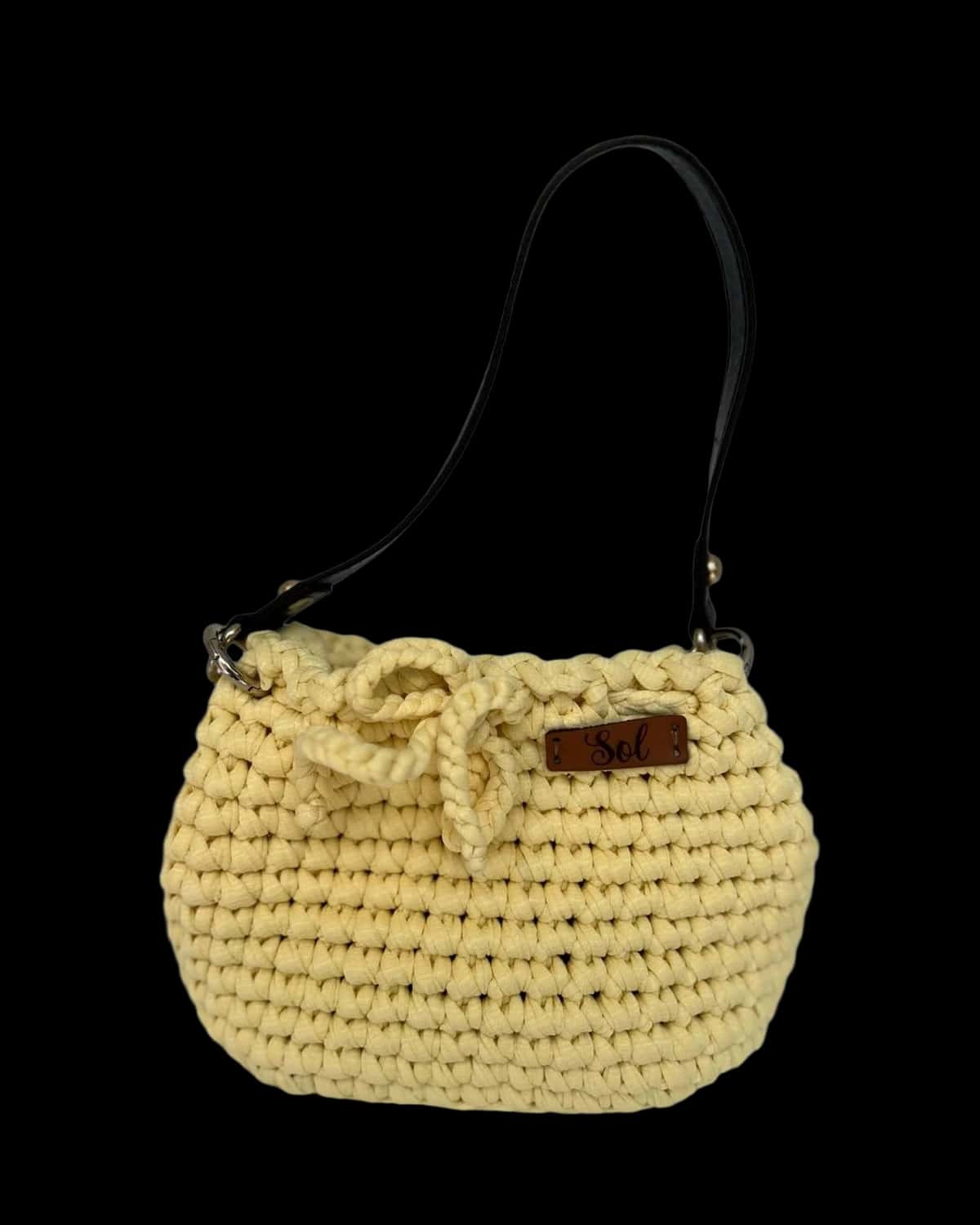 Bolsa infantil amarelo-claro com laço e alça tipo couro preta, foto de catálogo em fundo neutro