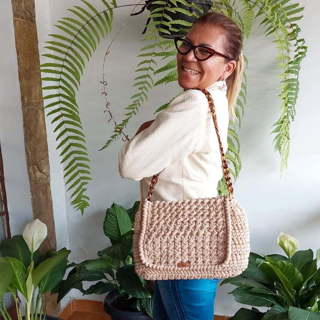 Cliente de blusa branca com a bolsa Genebra bege no ombro, entre samambaias