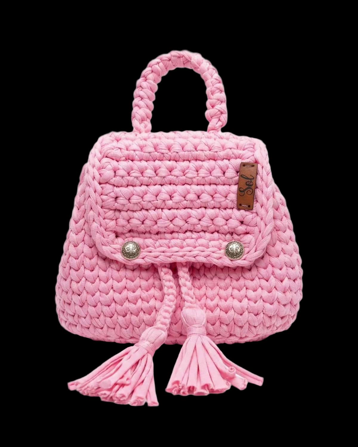 Mochila infantil rosa em crochê de fio de malha, com dois botões e tassels, foto de catálogo em fundo neutro