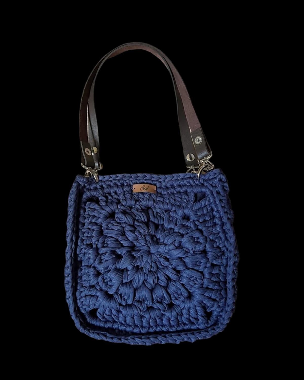 Bolsa Paris quadrada azul-marinho com flor de crochê em relevo e duas alças tipo couro, foto de catálogo em fundo neutro